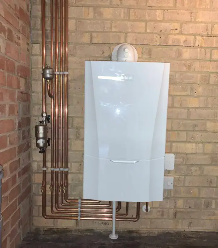 Modern white gas boiler with copper pipes on a brick wall in a residential setting.