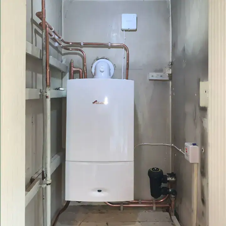 A boiler installed in a utility room with copper pipes and a control unit, suitable for heating and hot water systems.