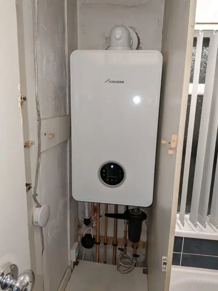 Worcester combi boiler installed in a utility area with exposed pipes and a white wall.