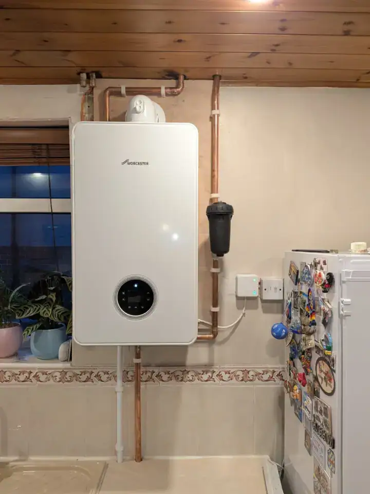 A modern Worcester boiler installed on a kitchen wall with copper pipes and a white fridge with magnets nearby.