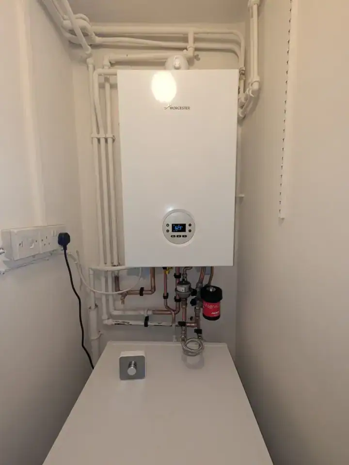 A modern Worcester Bosch combi boiler installed in a utility room with white walls and piping, for central heating and hot wa.