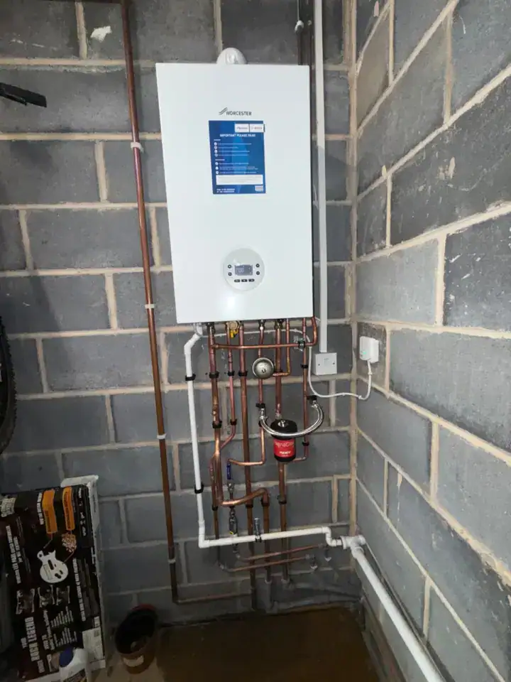 Gas boiler with copper pipework and pressure gauge installed on a brick wall in a utility room.