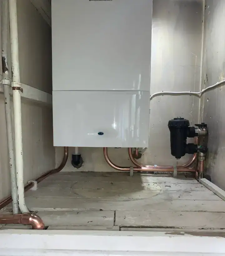 A boiler system with copper pipes and a black filter installed on a concrete floor in a utility room.