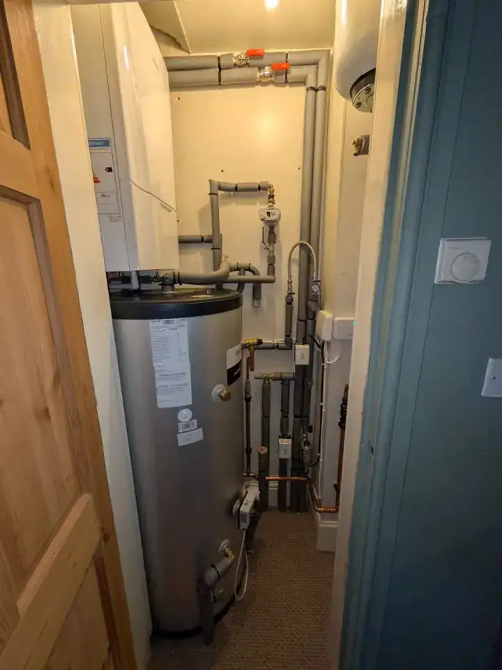 A boiler and pipework installation in a small utility room, with visible plumbing and heating components.
