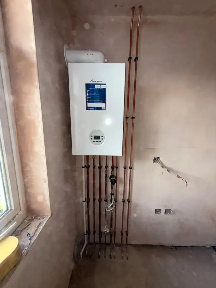 A boiler installation with copper pipes in a room under construction, wall-mounted heating system in progress.