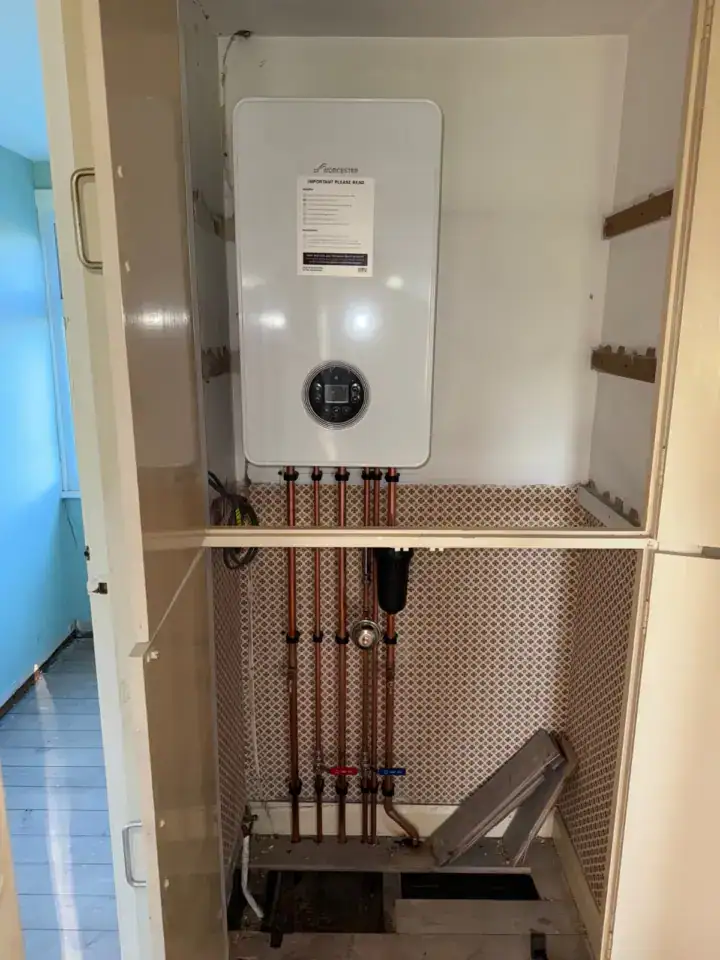 A gas boiler installed inside a kitchen cupboard with copper pipework and a control panel, ready for heating and hot water su.